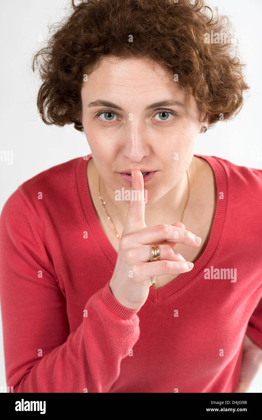 junge Frau mit lockigen Haaren und roten Pullover mit Finger vor den Lippen Stockfoto