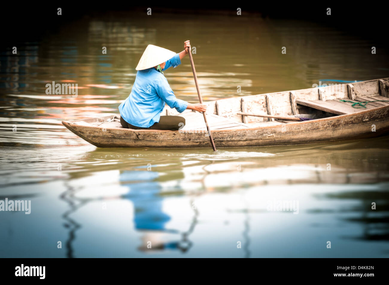 Frau in konische Hut sitzt auf Kanu und Rudern. Traditionelle asiatische Boot aus Holz gebaut. Person Paddel in den Händen halten. Welligkeit auf Stockfoto
