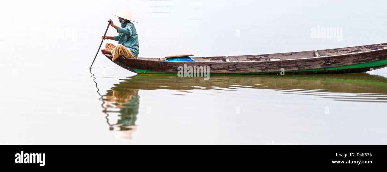 Frau in konische Hut sitzt auf Kanu und Rudern. Traditionelle asiatische Boot aus Holz gebaut. Person Paddel in den Händen halten. Welligkeit auf Stockfoto