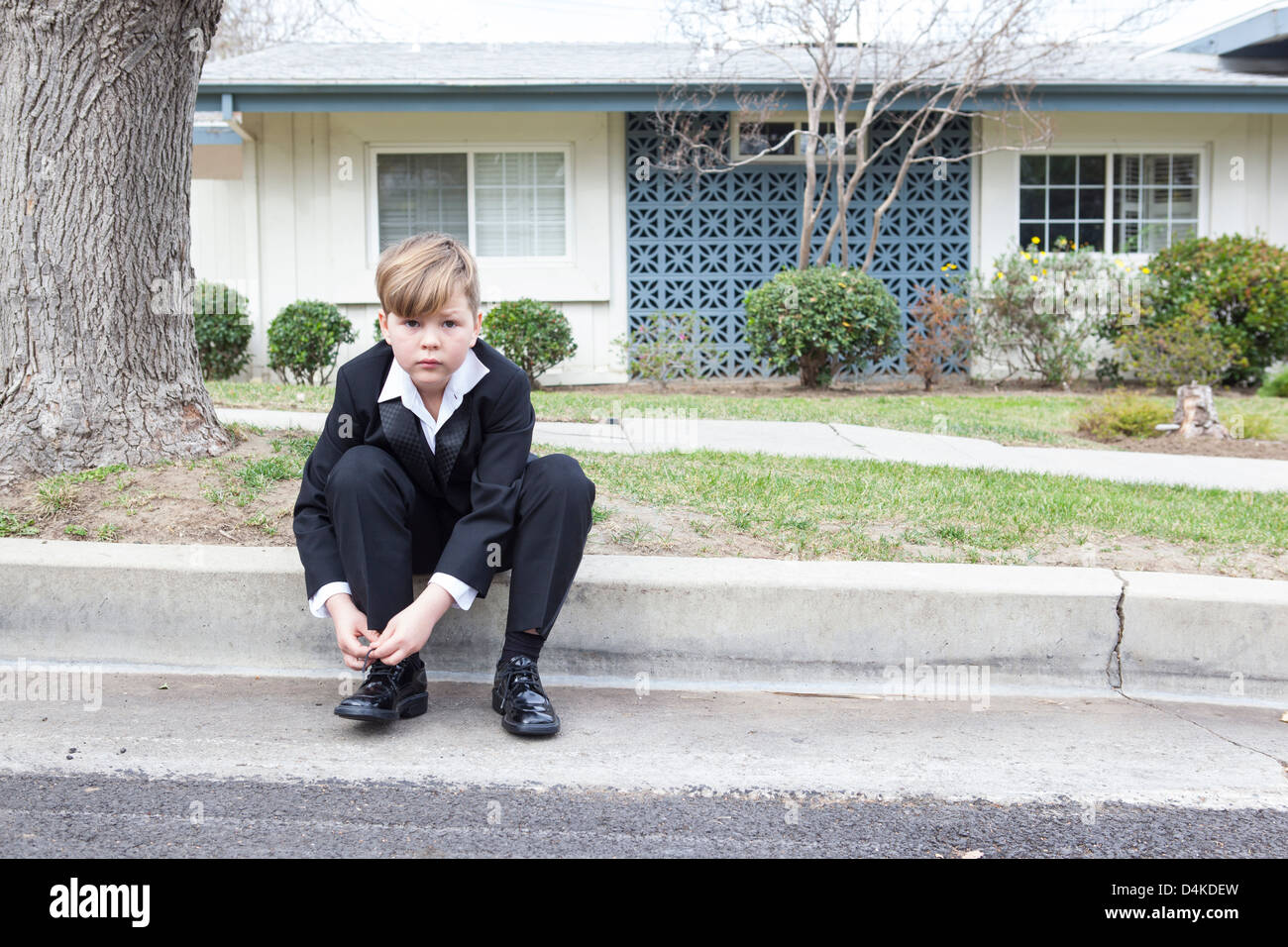Junge im Anzug sitzt auf Vorort Straße Stockfoto