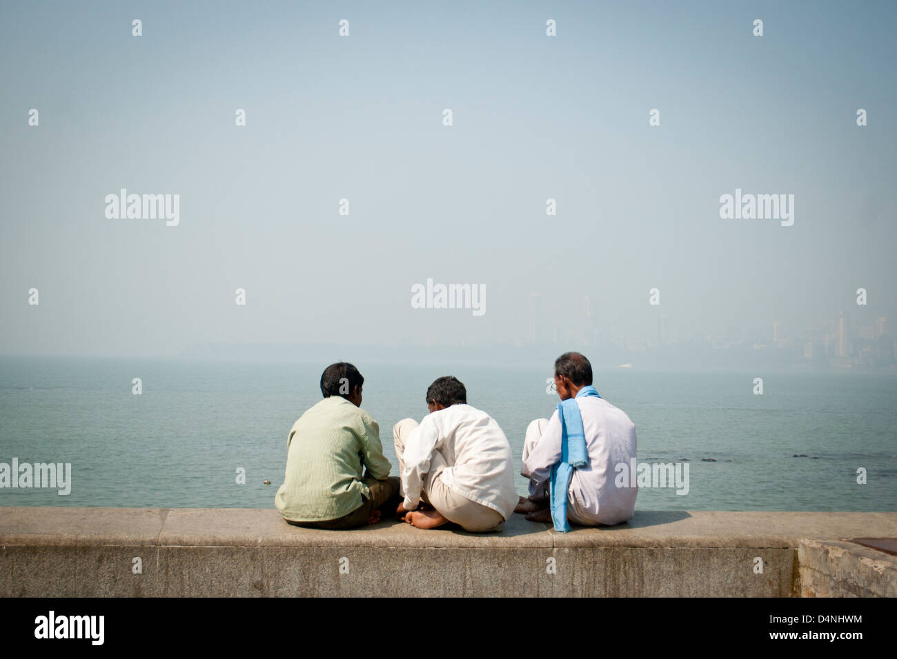 Drei indische Männer sitzen auf dem Deich mit Blick auf das Arabische Meer am Chowpatti Beach, Mumbai, Indien Stockfoto