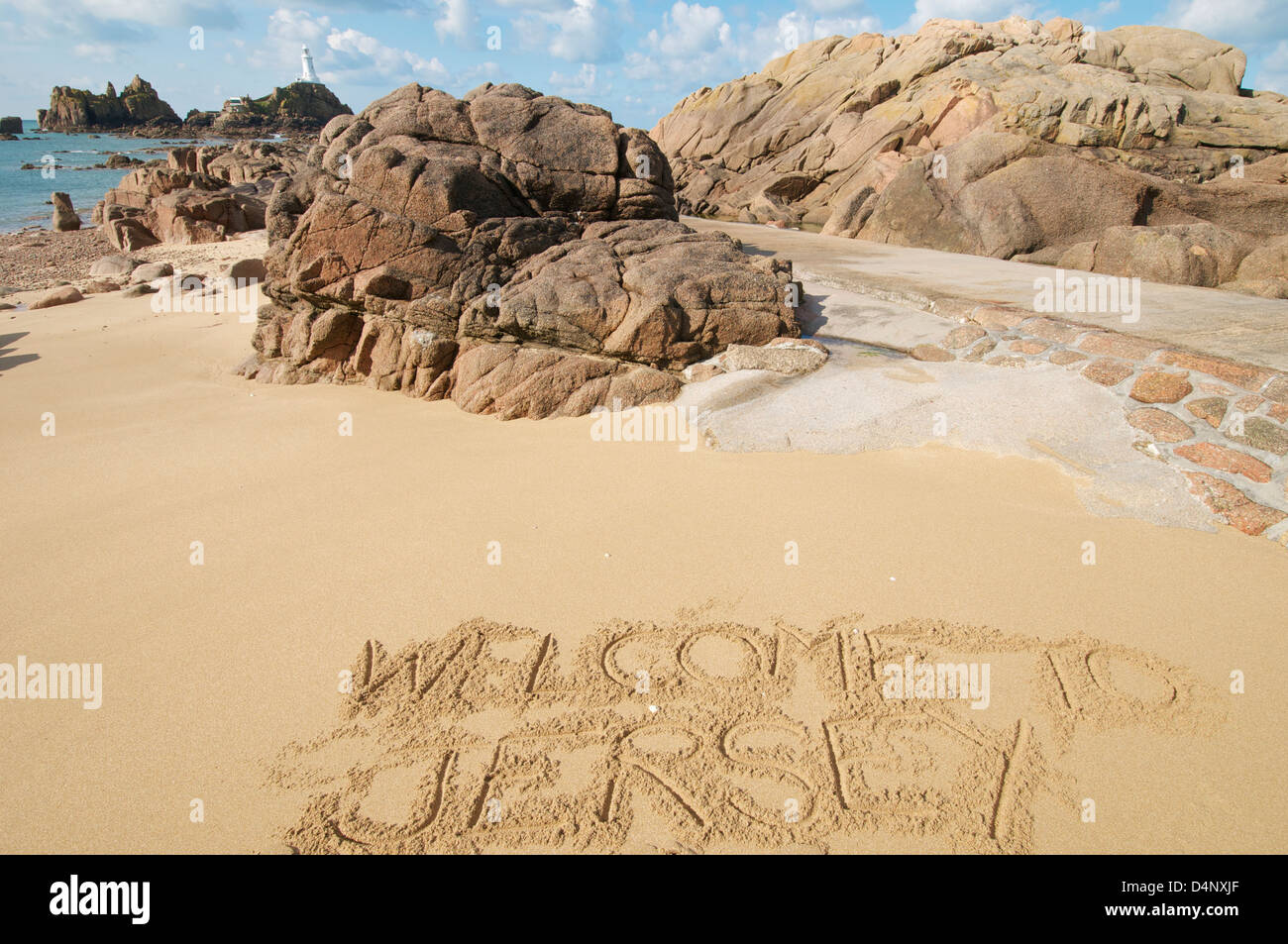 Bild der Corbiere Leuchtturm Jersey Channel Islands mit Flut, März 2013 und herzlich willkommen auf Jersey in den Sand geschrieben Stockfoto