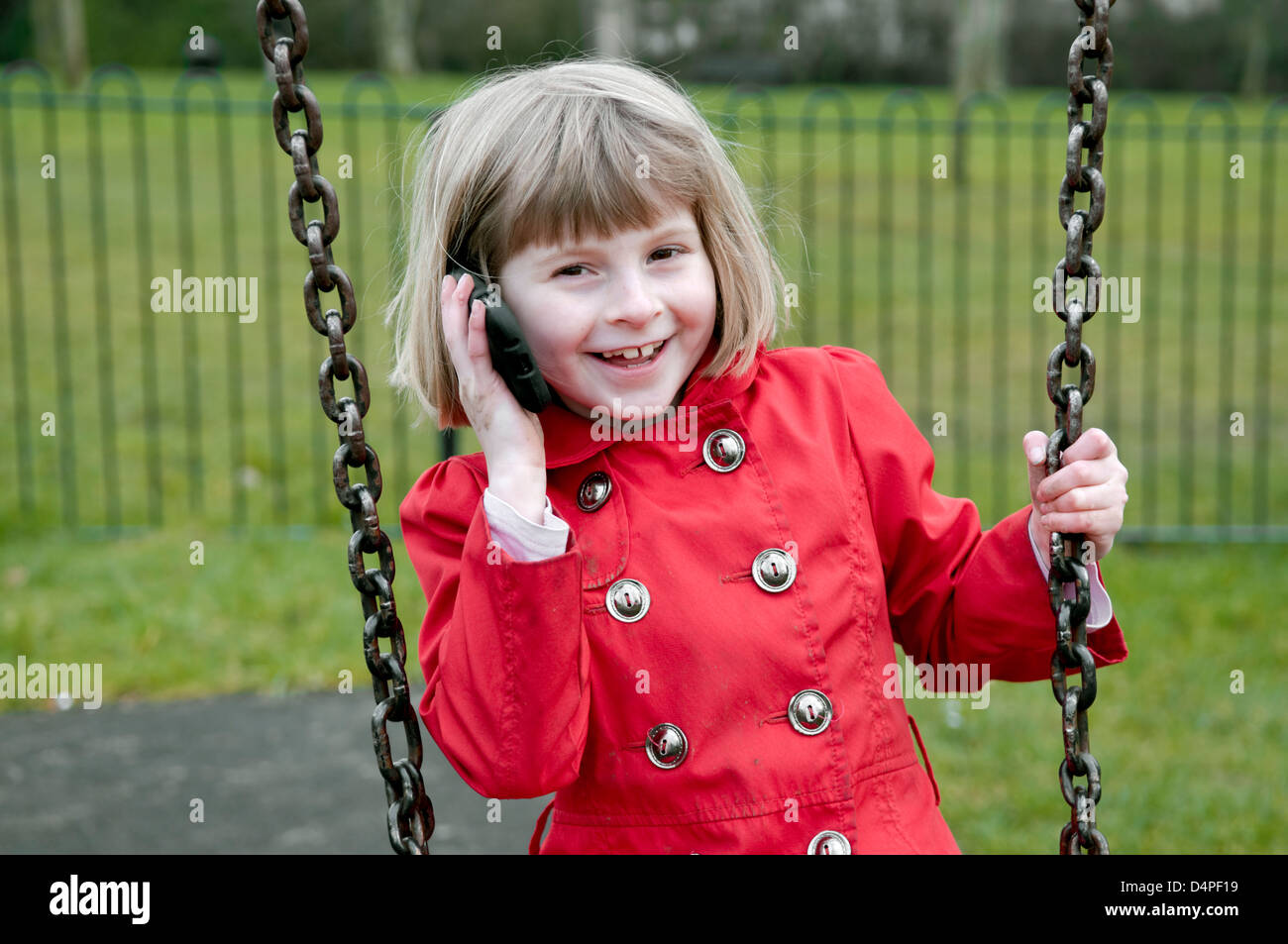 8 Jahre alte kaukasische Mädchen Lachen und telefonieren mit Handy während sagen auf der Schaukel. Stockfoto