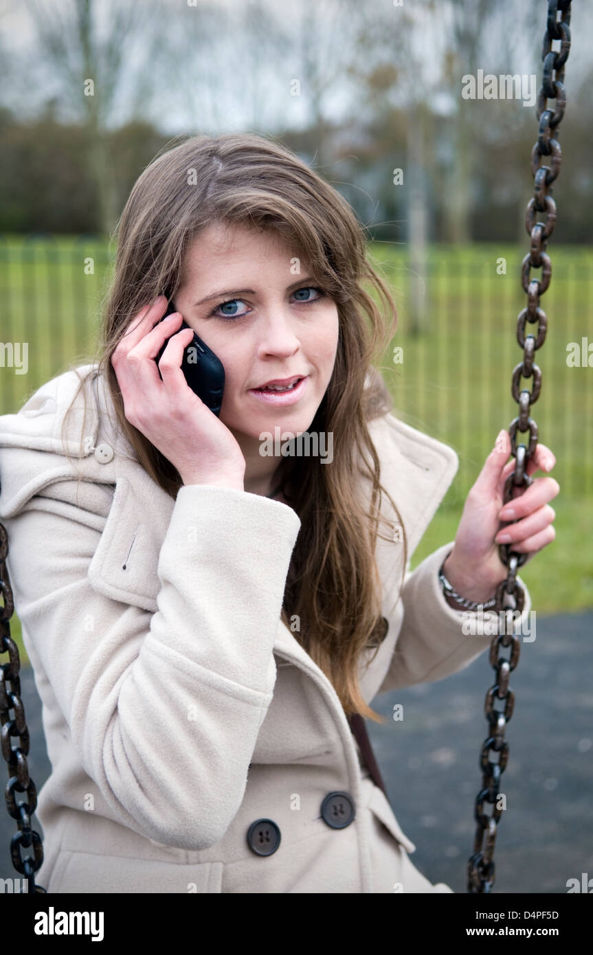 Attraktive junge kaukasischen Frau am Handy auf Schaukel im Park in Bristol, Großbritannien Stockfoto