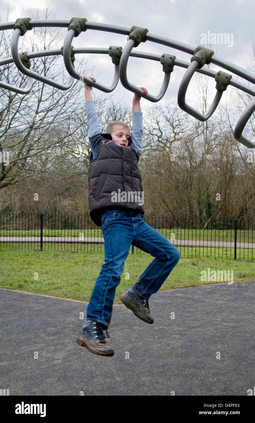 10 Jahre alten kaukasischen jungen schwingen über Klettergerüst im Park in Bristol, UK Stockfoto