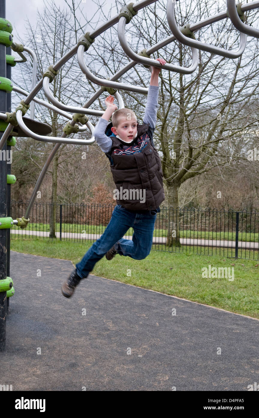 10 Jahre alten kaukasischen jungen schwingen über Klettergerüst im Park in Bristol, UK Stockfoto