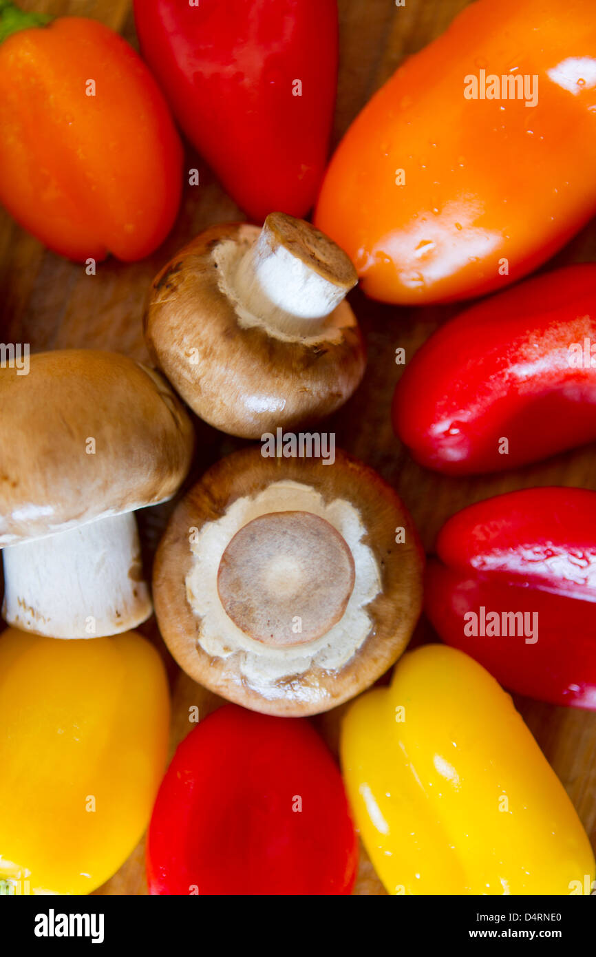 Pilze und bunte Paprika werden momentan auf einem nassen Bambus Schneidbrett abgeschnitten. Stockfoto