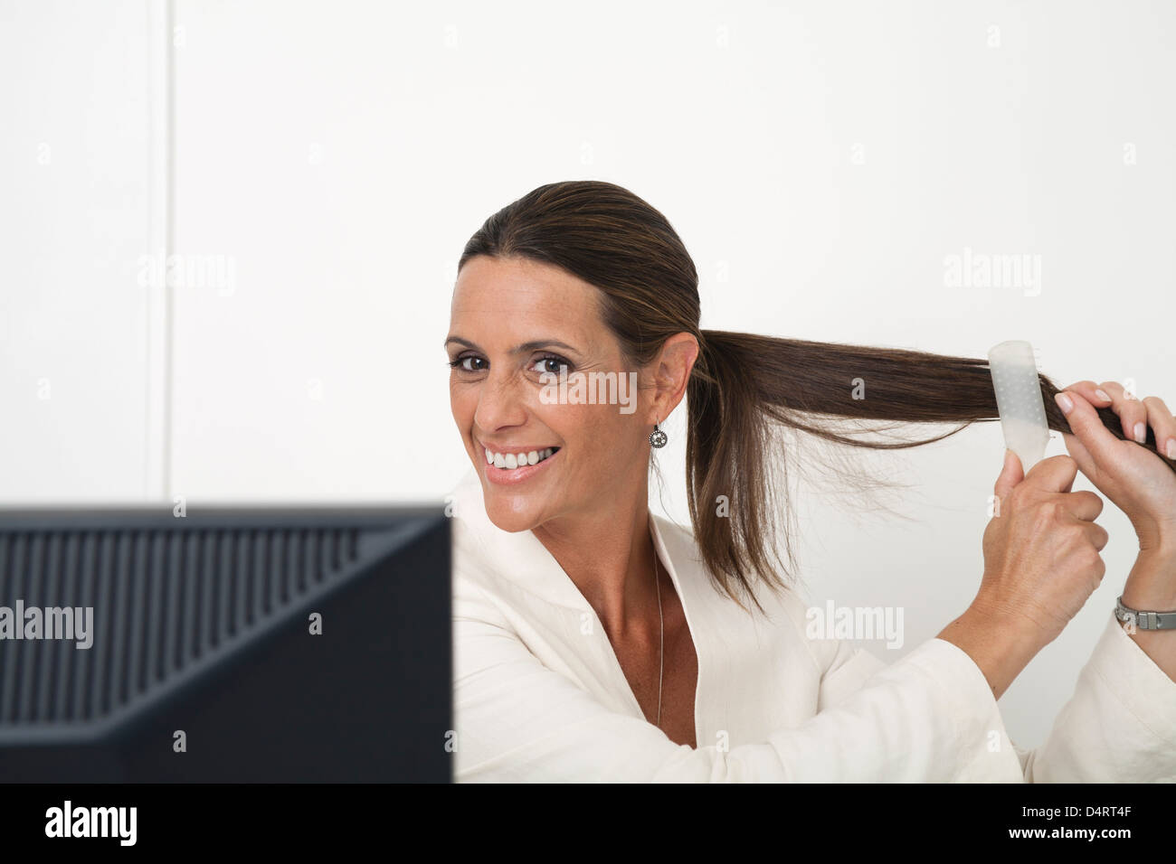 Reife Geschäftsfrau Bürsten Haare am Schreibtisch Stockfoto