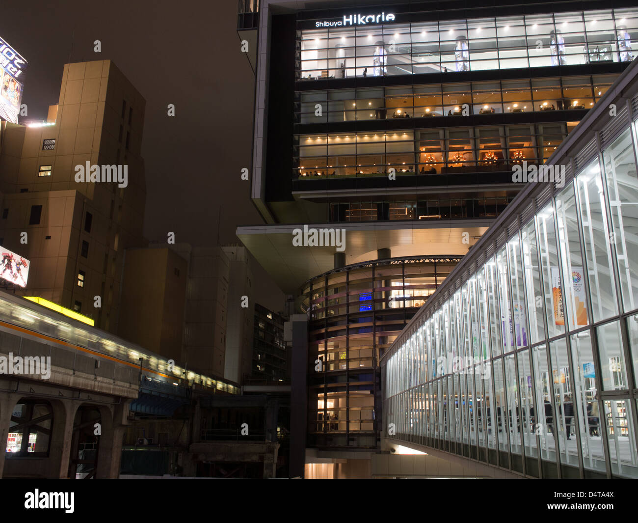 Tokio bei Nacht. Ein Zug der Ginza-Linie reist in Richtung Shibuya Station neben dem Fußgängerweg zum Hikarie Gebäude. Stockfoto