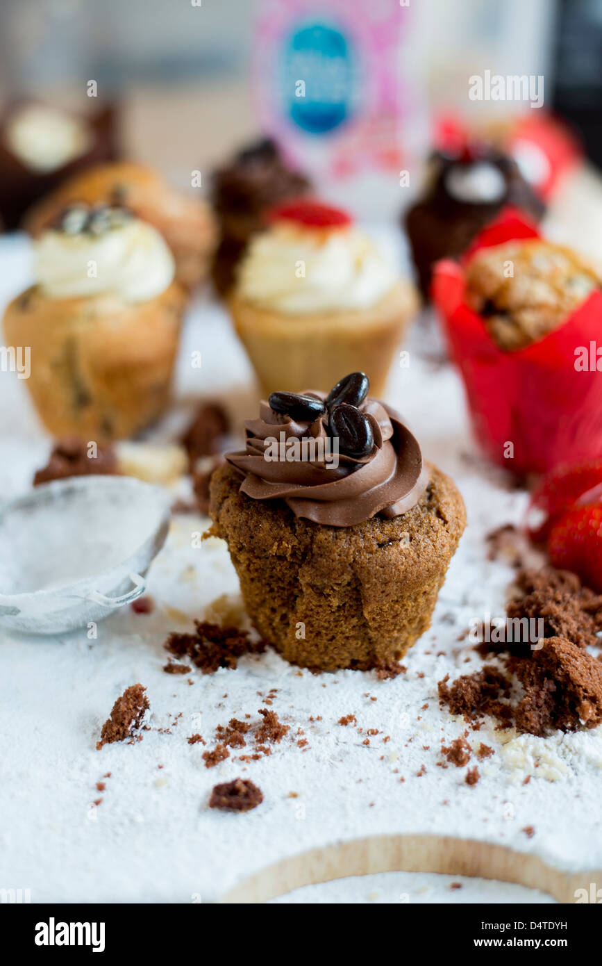 Ein Schokoladen-Kaffee-Muffin, umgeben von Krümel mit anderen Muffins im Hintergrund Stockfoto