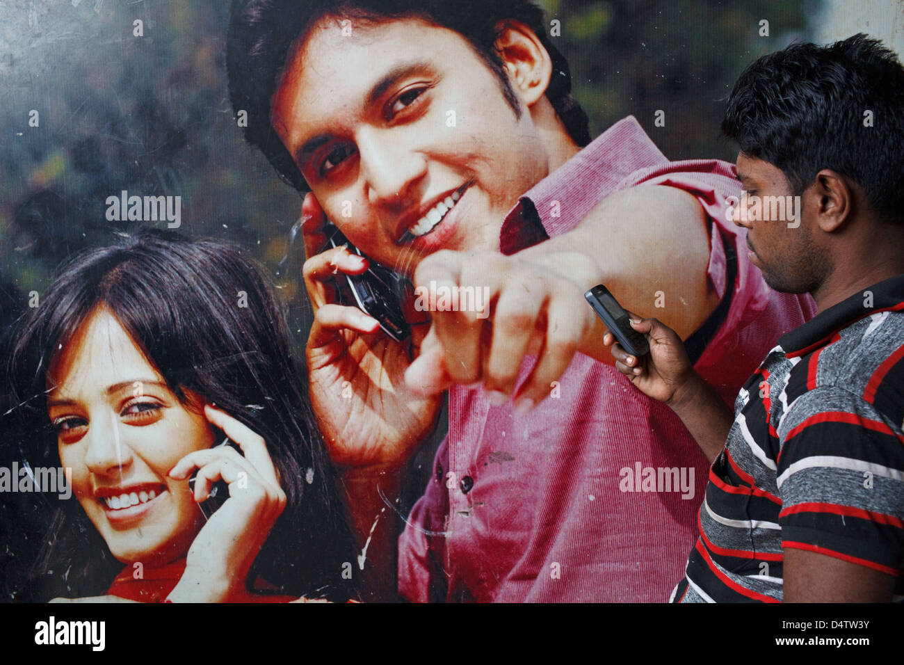 Ein Bangladeshi Mann mit dem Handy telefonieren mit einer Handy-Firma Werbung als Kulisse in Dhaka, Bangladesch. Stockfoto