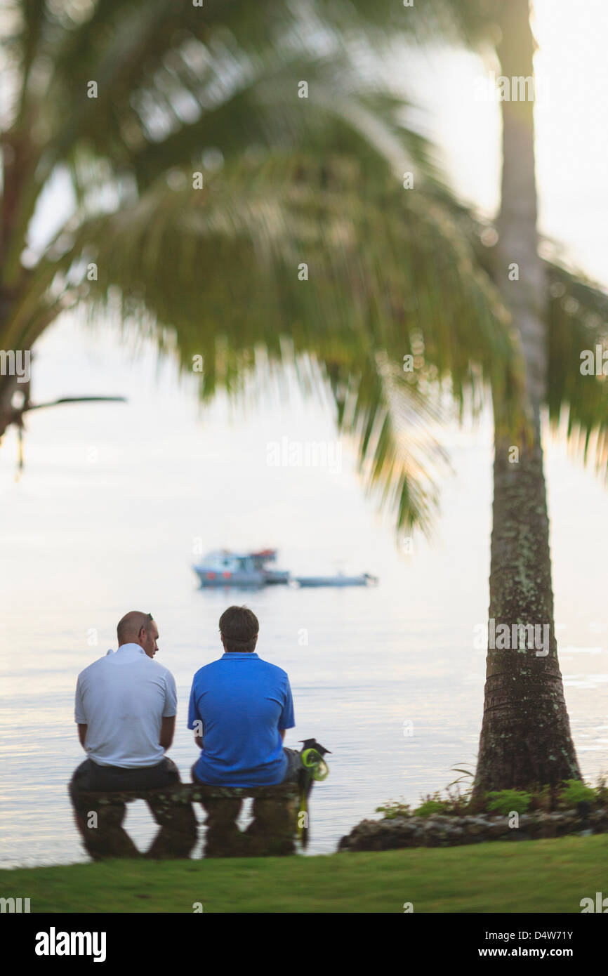 Männer sitzen unter Palmen am Strand Stockfoto