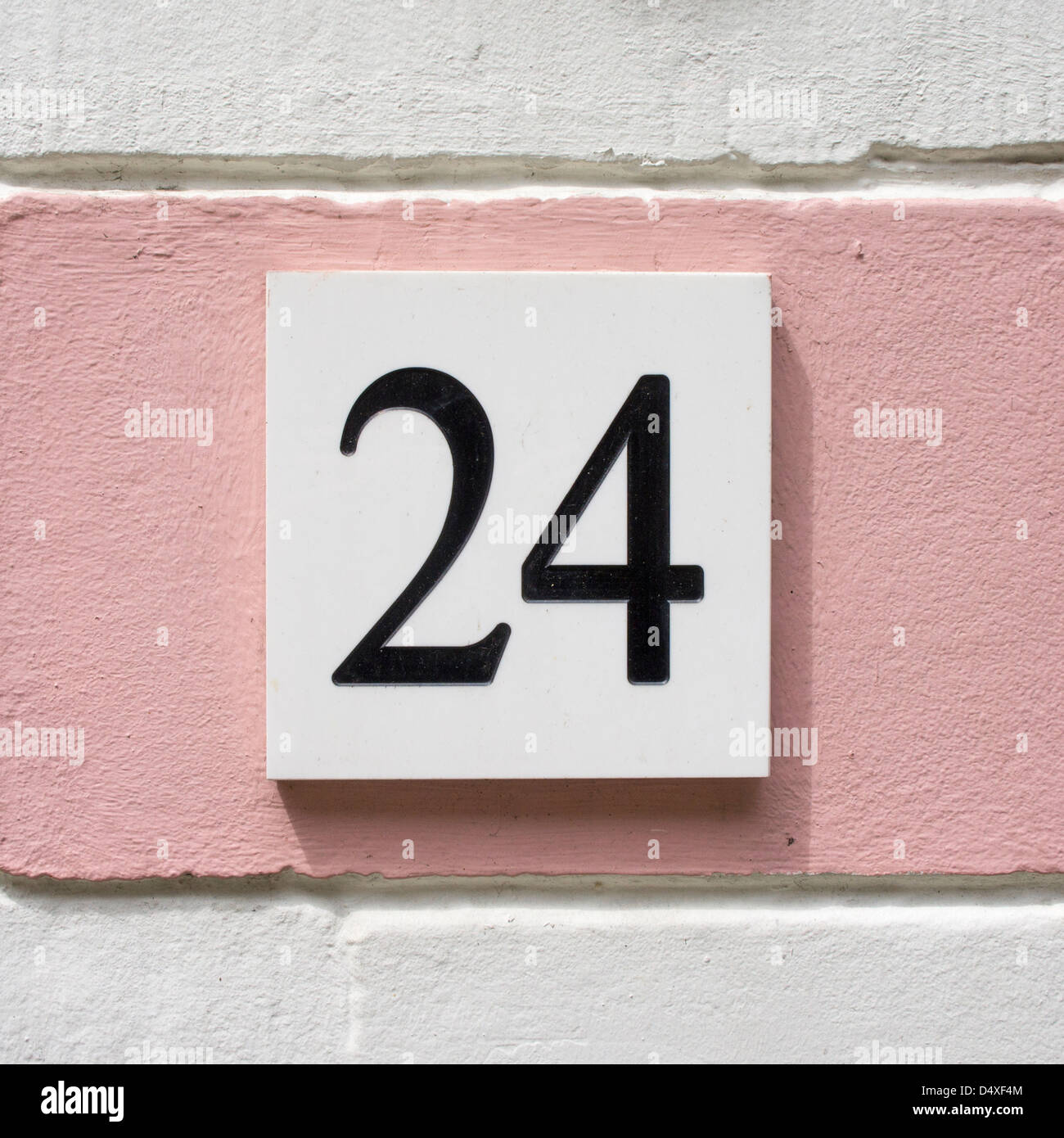 Hausnummer 24. Schwarzer Schrift auf einem weißen Teller auf einer rosa Wand. Stockfoto