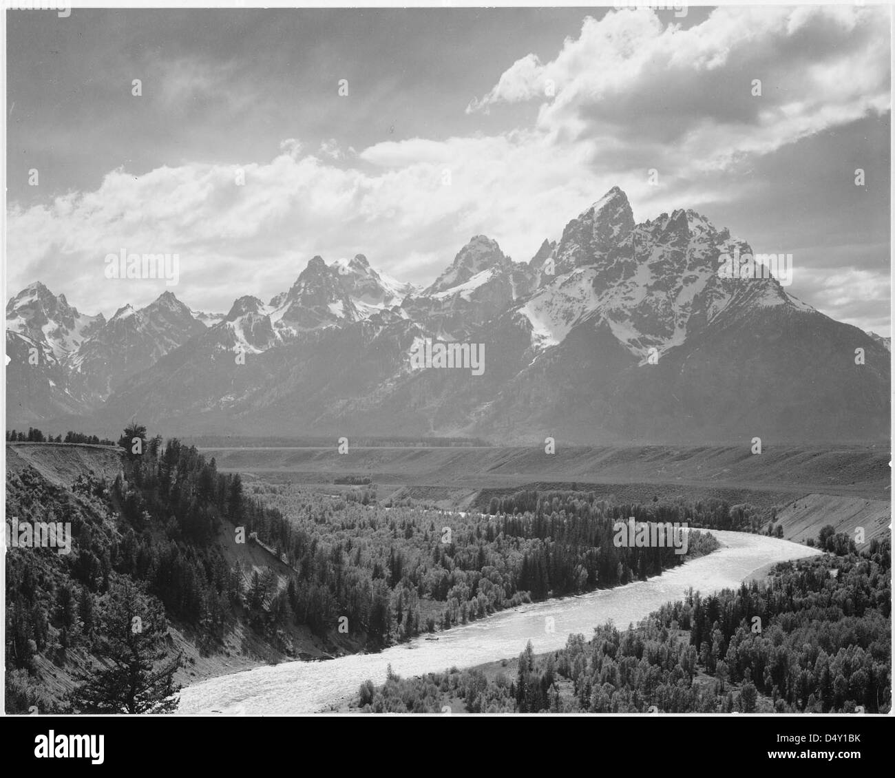 Ein Foto des Grand Teton National Park, Wyoming, von Ansel Adams, das einen Fluss zeigt, der durch das Tal fließt, mit schneebedeckten Bergen im Hintergrund. Die Aussicht fängt die raue Schönheit der Region ein. Stockfoto