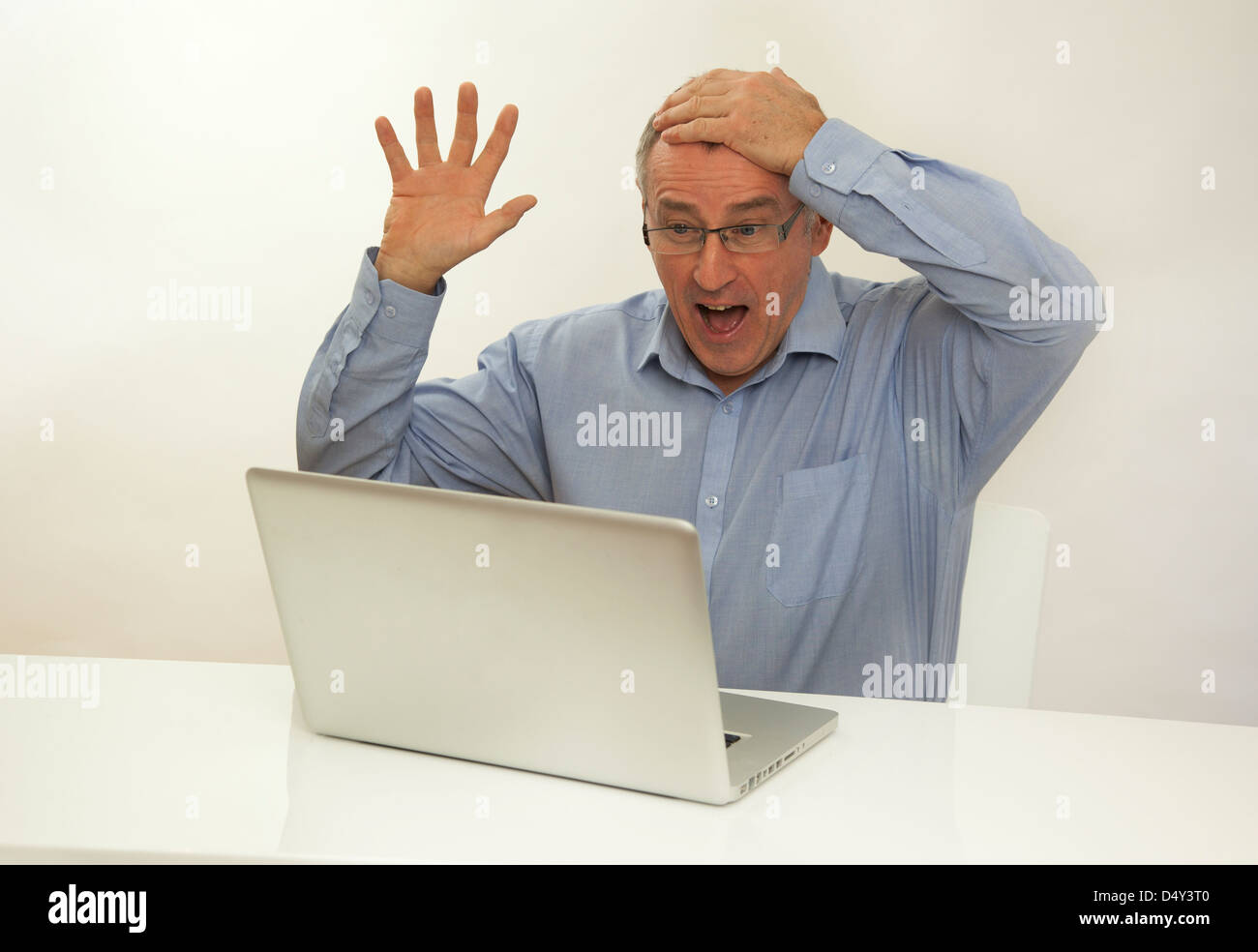 Überglücklich Mann hand auf Kopf mit Blick auf einem Laptop-Bildschirm, froh, dass er einen Preis gewonnen hat. Stockfoto