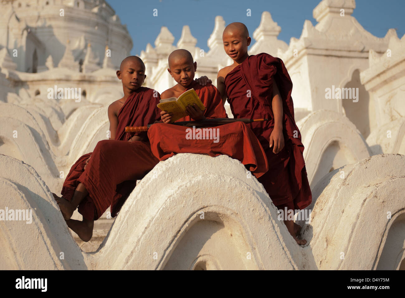 drei junge Mönche beim Sitzen auf der Klostermauern in Birma auch bekannt als Myanmar lesen Stockfoto