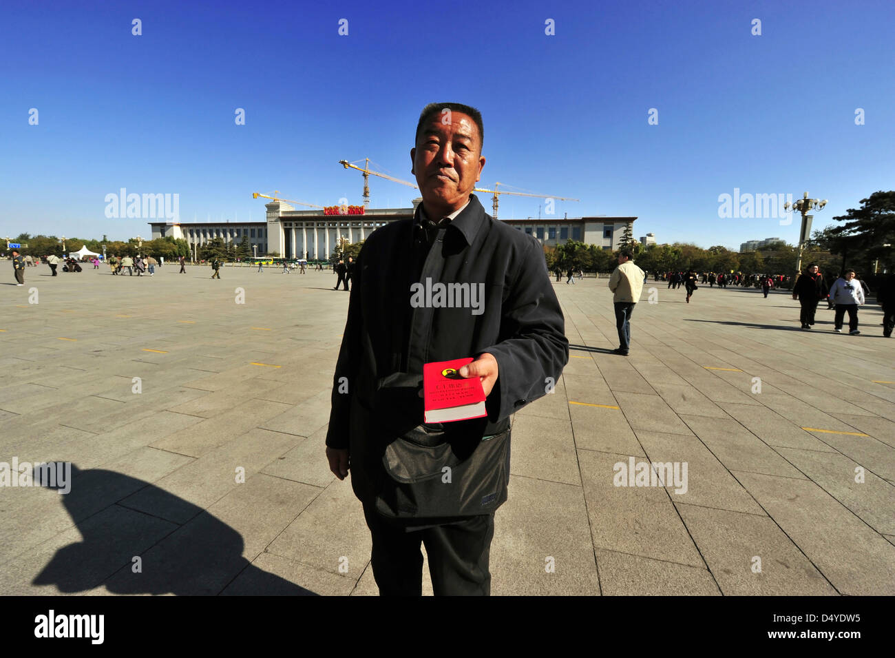 China, Beijing, Mann im Mantel hält ein wenig rotes Buch von Mao mit Gebäude im Hintergrund Stockfoto