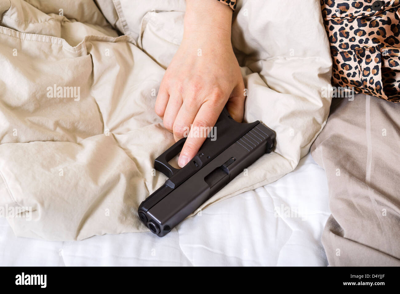 Horizontale Foto von weiblicher Hand, die persönliche Waffe, Pistole, während im Bett Stockfoto