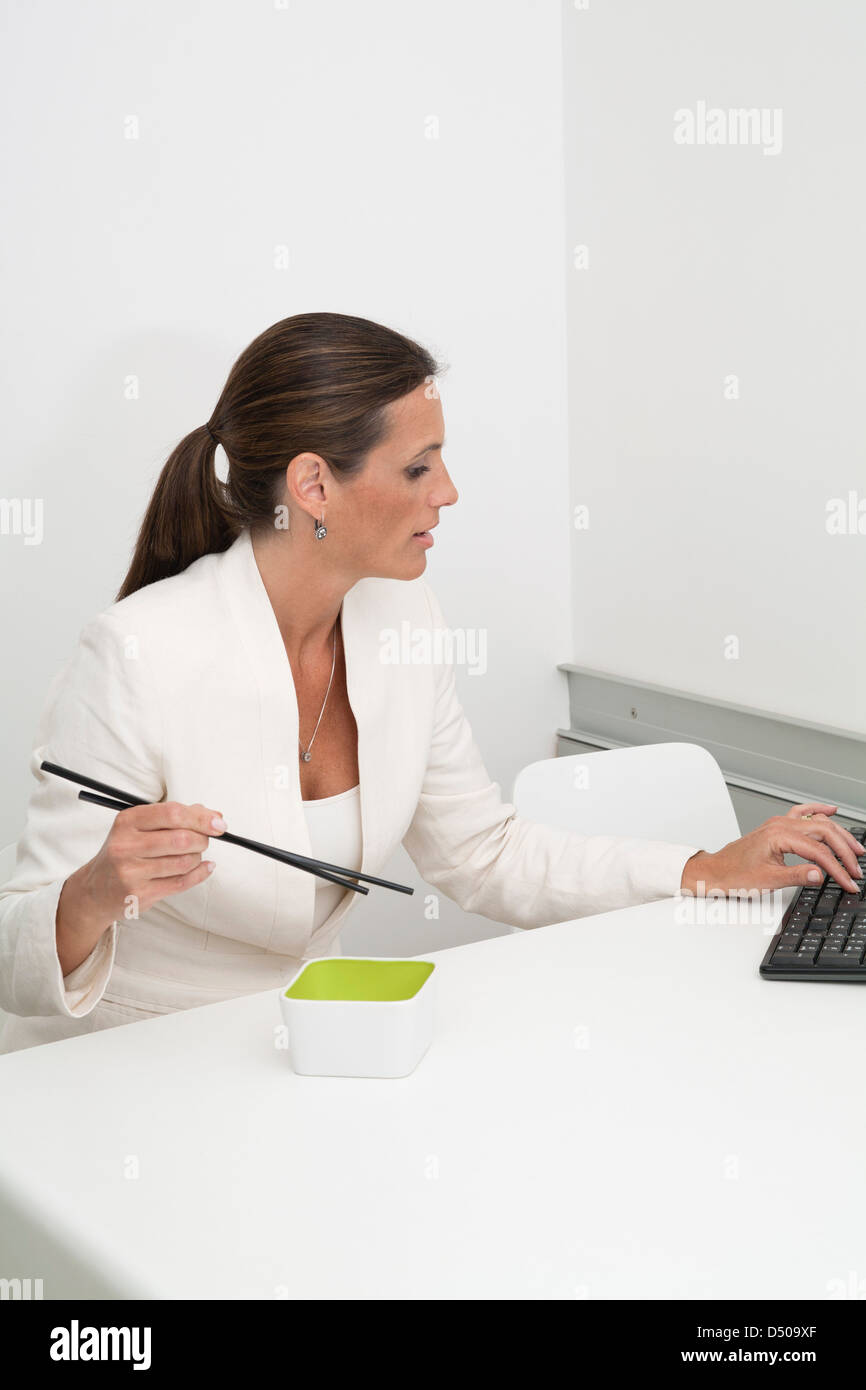 Reife Geschäftsfrau, Essen mit Stäbchen am Schreibtisch Stockfoto