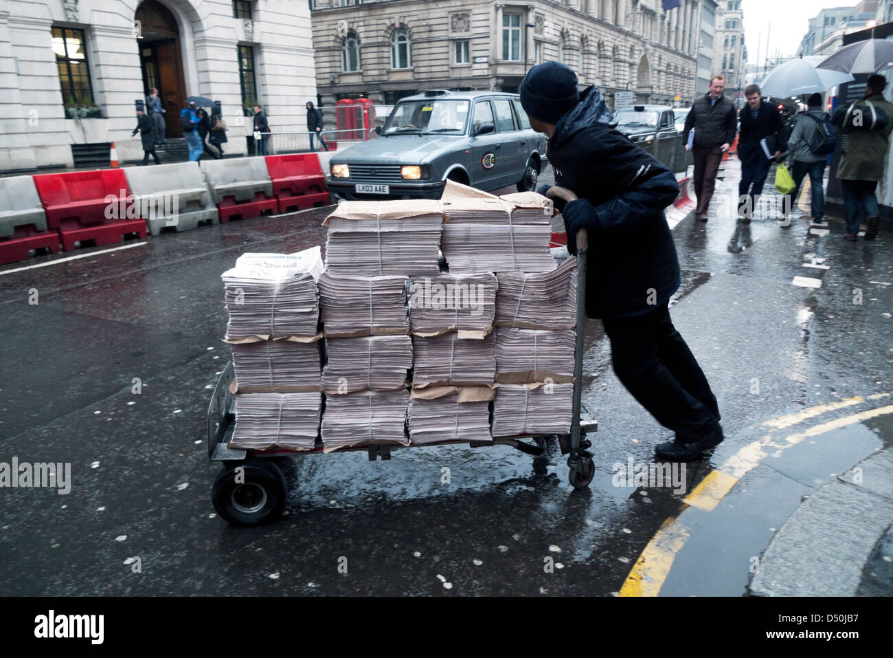 Eine Zeitung Verkäufer Arbeitskraft liefern einen Stapel Zeitungen im Regen an einem Zeitungsstand in Moorgate London England UK KATHY DEWITT Stockfoto