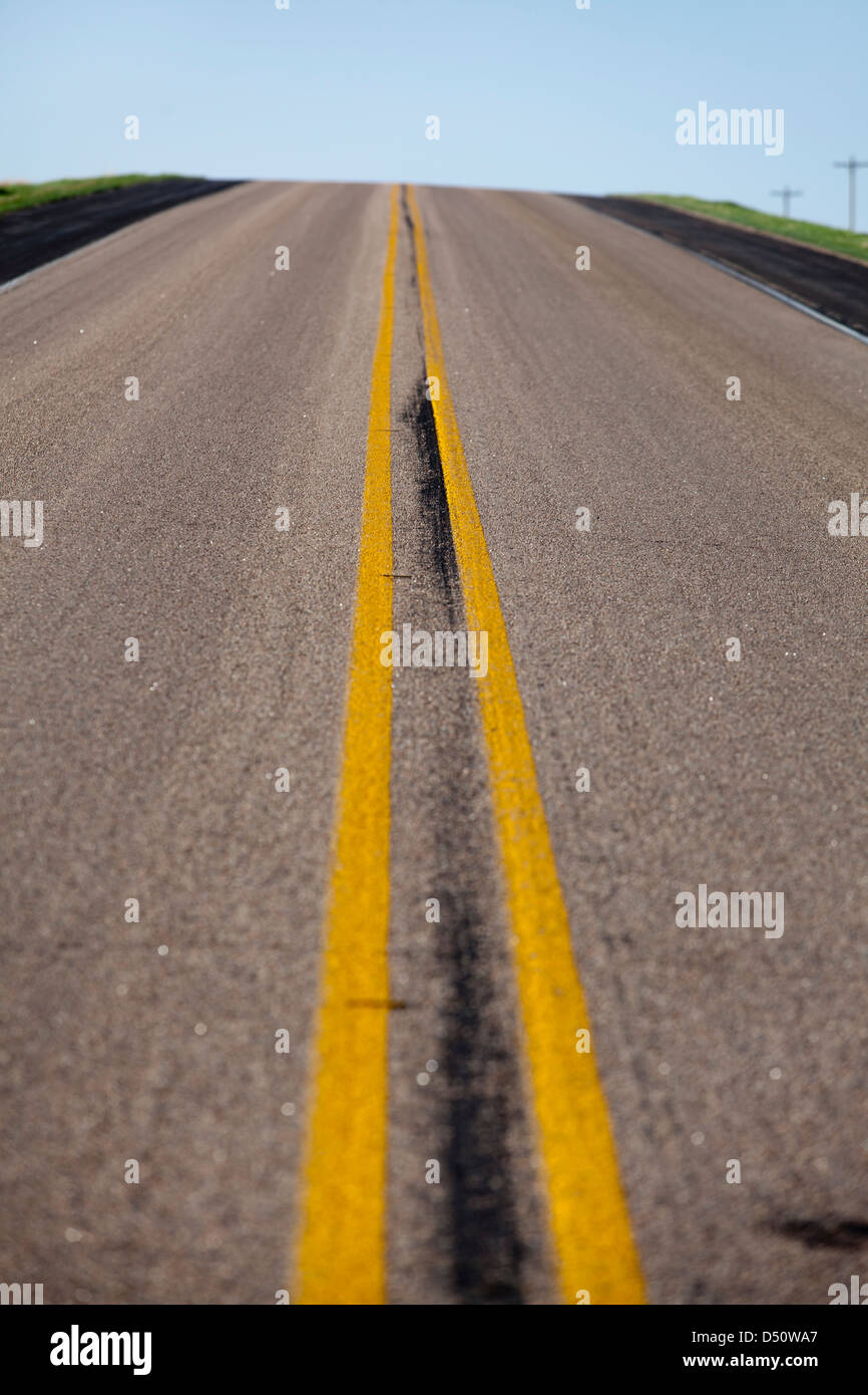 Eine verlassene Straße mit doppelten gelbe Linie und blauem Himmel in Oklay, Kansas, USA Stockfoto