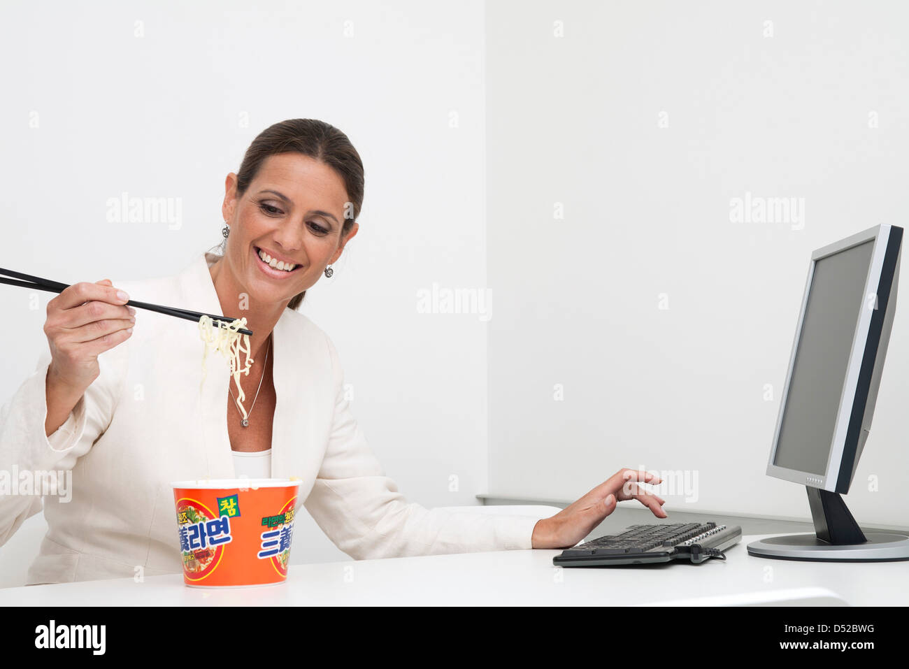Reife Geschäftsfrau instant-Nudeln zu essen, am Schreibtisch Stockfoto