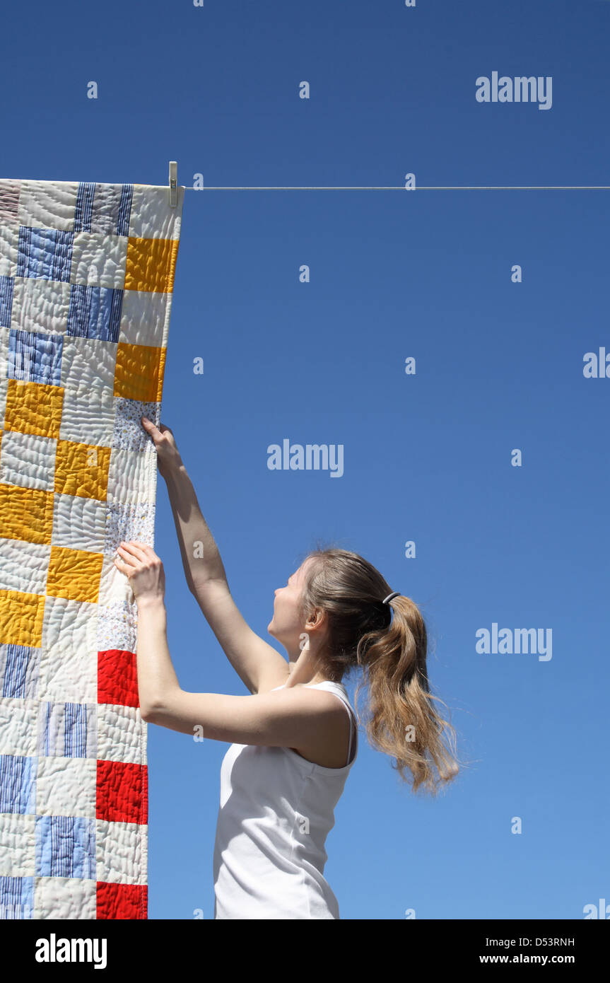 Junge Frau berühren eine helle Patchwork Bettdecke hängen auf einer Wäscheleine trocknen. Stockfoto