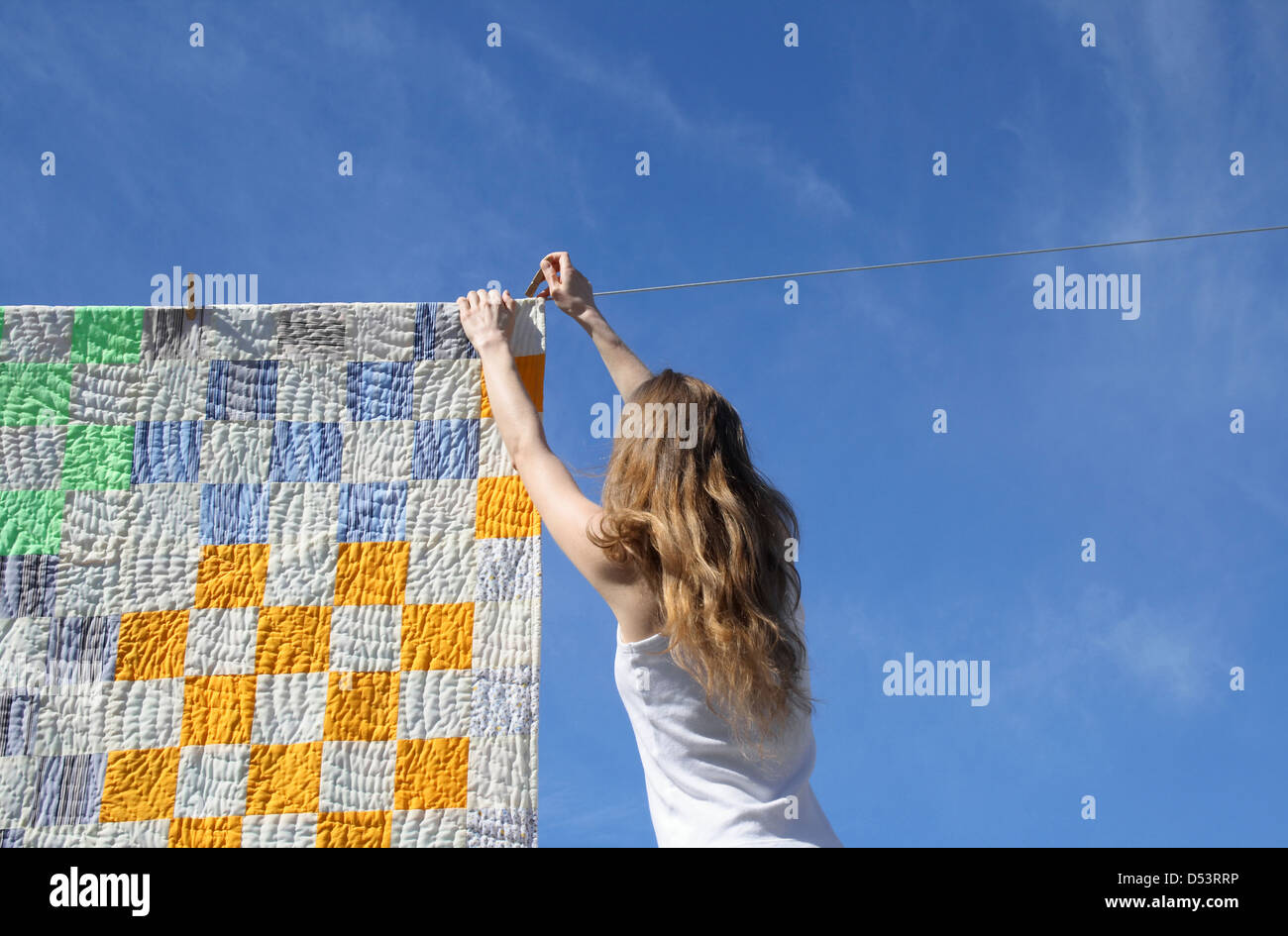Langhaarige junge Frau, eine helle Bettdecke auf eine Wäscheleine zum Trocknen in ein Kinderspiel. Stockfoto