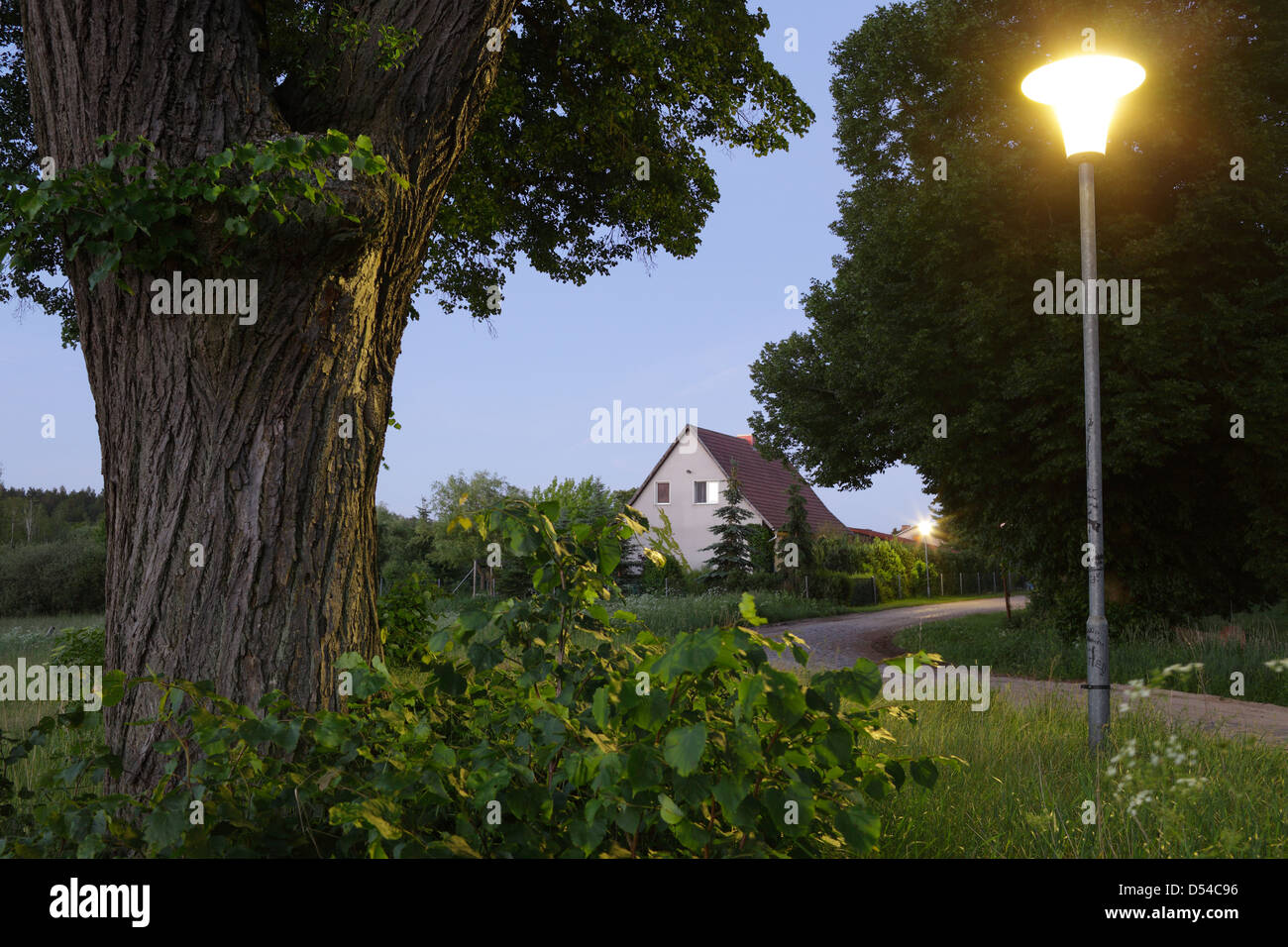 Metzelthin, Deutschland, Dorfstraße, Haus und Straßenlaterne in der Abenddämmerung Stockfoto
