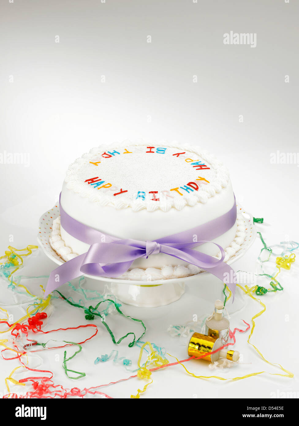Eine weiße Zuckerglasur Kuchen auf eine Tortenplatte mit lila Schleife und Luftschlangen auf weißem Hintergrund Stockfoto