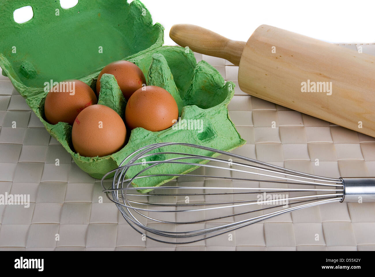 vier Eiern, Ballon Schneebesen und Nudelholz auf einer Bambusmatte Ort Stockfoto