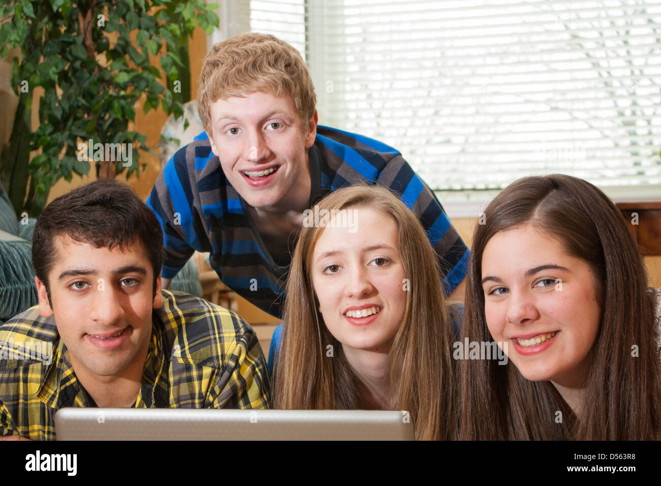 Eine heterogene Gruppe von Teenagern versammelten sich um einen Laptop in häuslicher Umgebung in die Kamera schaut Stockfoto