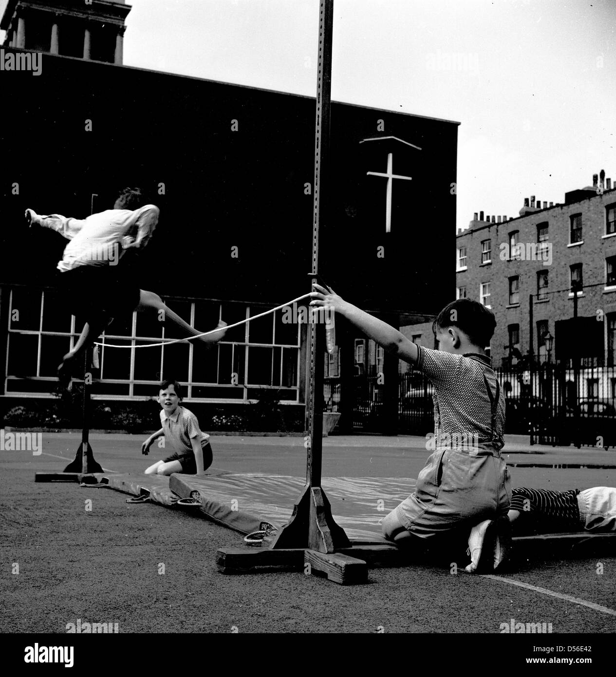 Historische 1950er. Schule der Leibeserziehung. Junge über ein Seil auf einer Matte auf dem Spielplatz, London, England, UK springen. Stockfoto