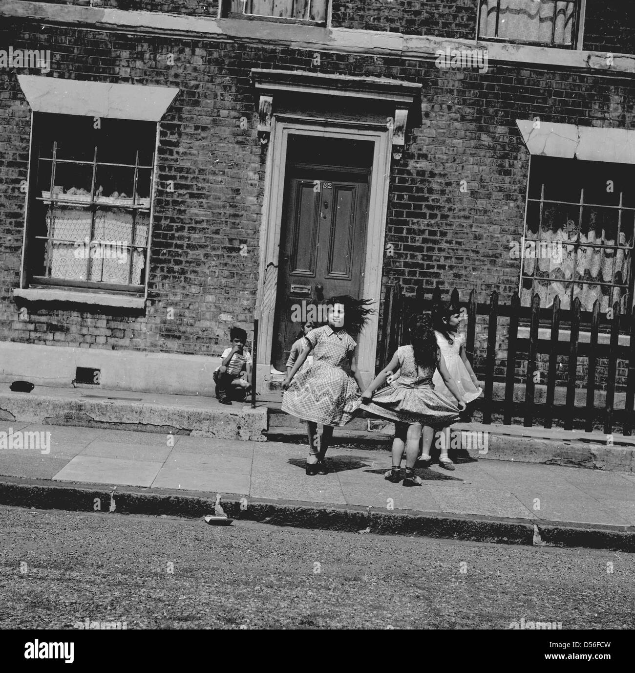 Historische der 1950er Jahre. Straße spielen. Junge Mädchen spielen - skipping - auf dem Bürgersteig vor einem viktorianischen Reihenhaus. Stockfoto