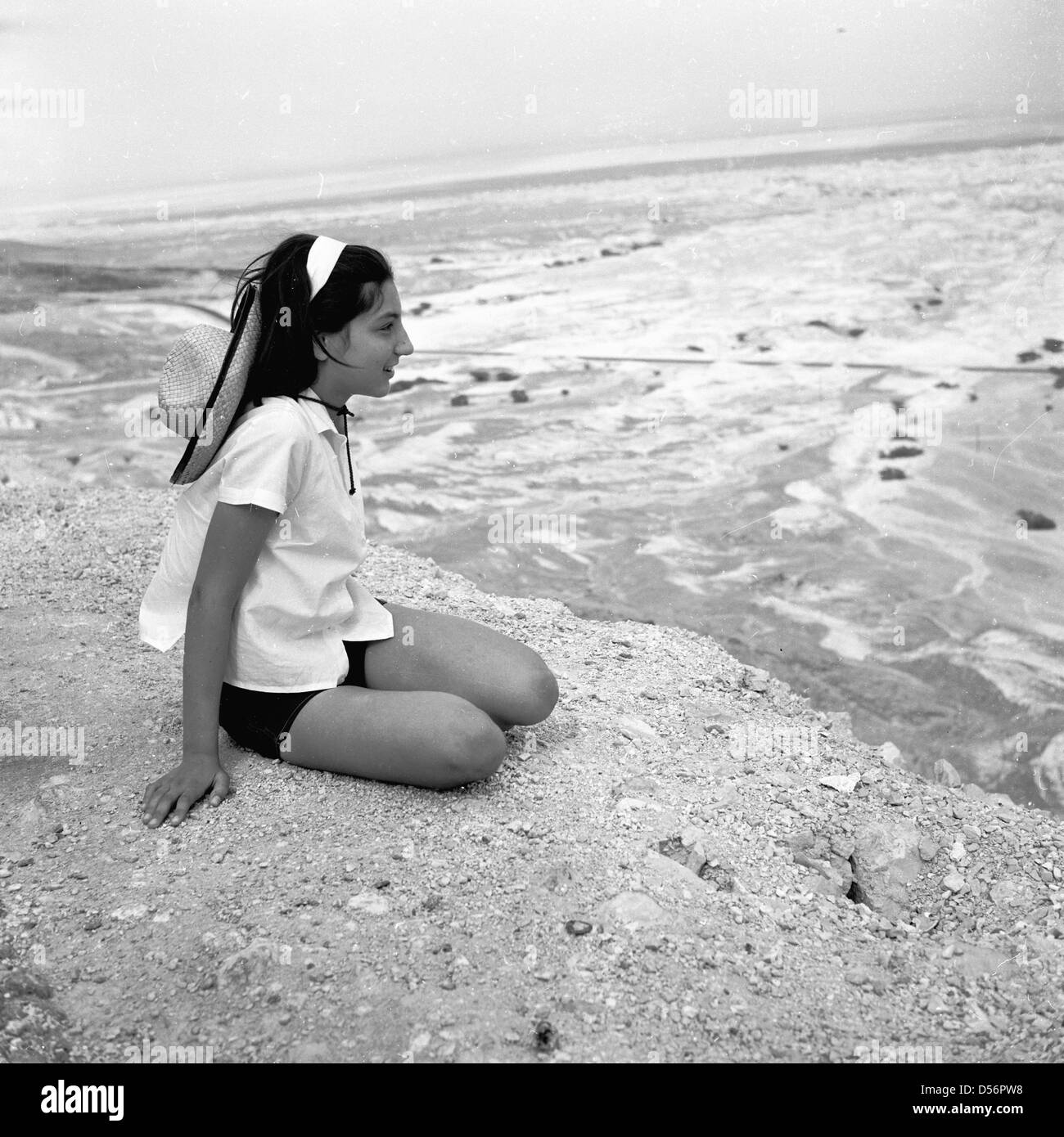 Israel, 1950er Jahre. Historisches Bild von einem jungen jüdischen Mädchen sitzt auf einem Felsen mit Blick auf die Wüste. Stockfoto