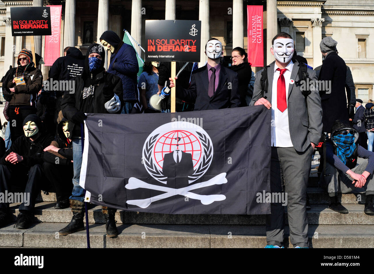 Eine Gruppe von Demonstranten, einige von ihnen tragen anonyme Masken auf einer Kundgebung auf dem Trafalgar Square, London, UK. Stockfoto