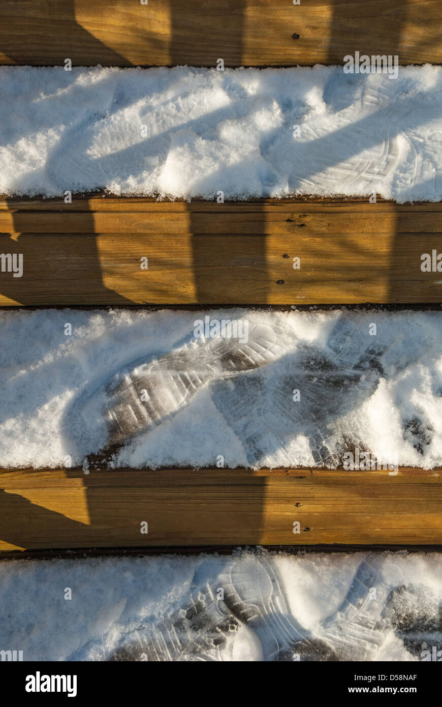 Licht und Schatten fallen gegen die horizontalen Streifen von Fußspuren auf verschneiten Holzstufen. Stockfoto