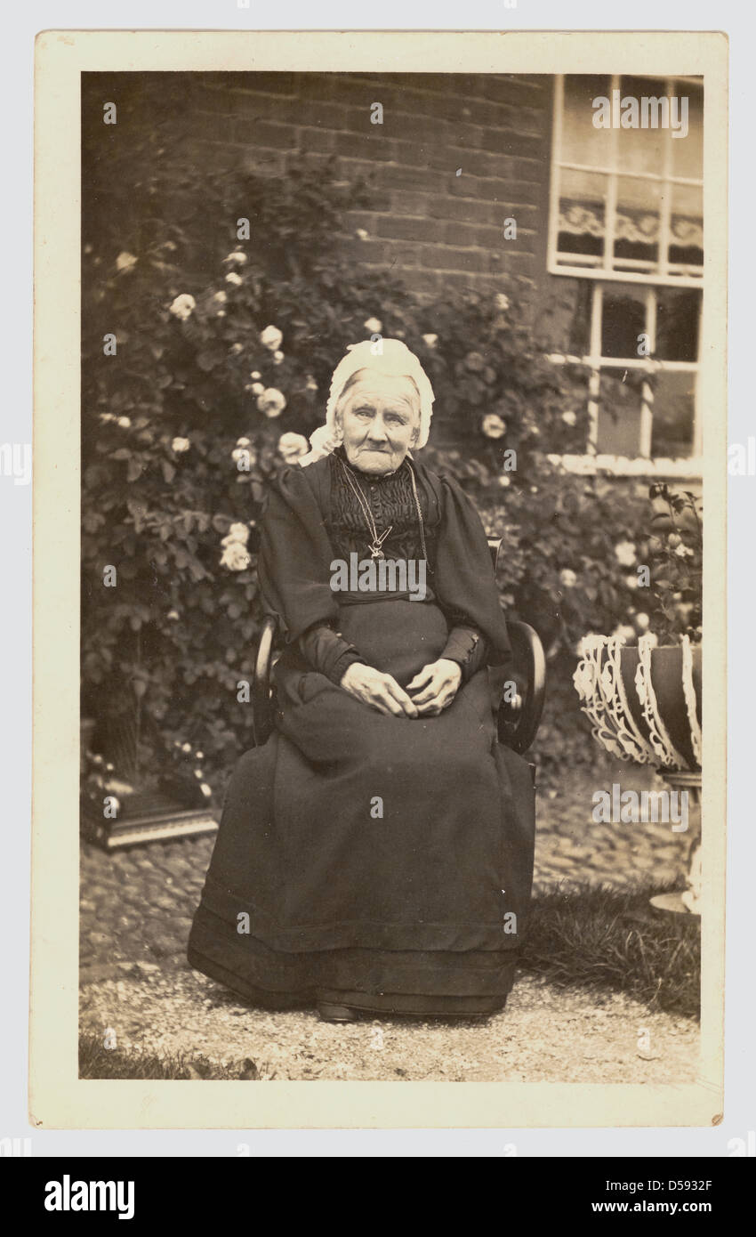 Postkarte von einer älteren Frau Edwardian sitzen vor ihrem Haus trägt eine Spitze Mütze, ca. 1905, U.K Stockfoto