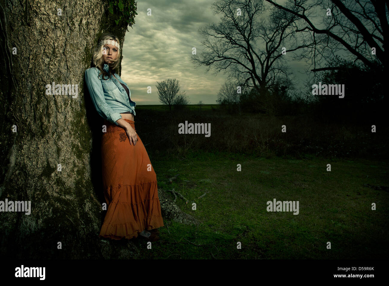 Blonde Frau lehnte sich gegen Baum im Park oder auf dem Land Stockfoto