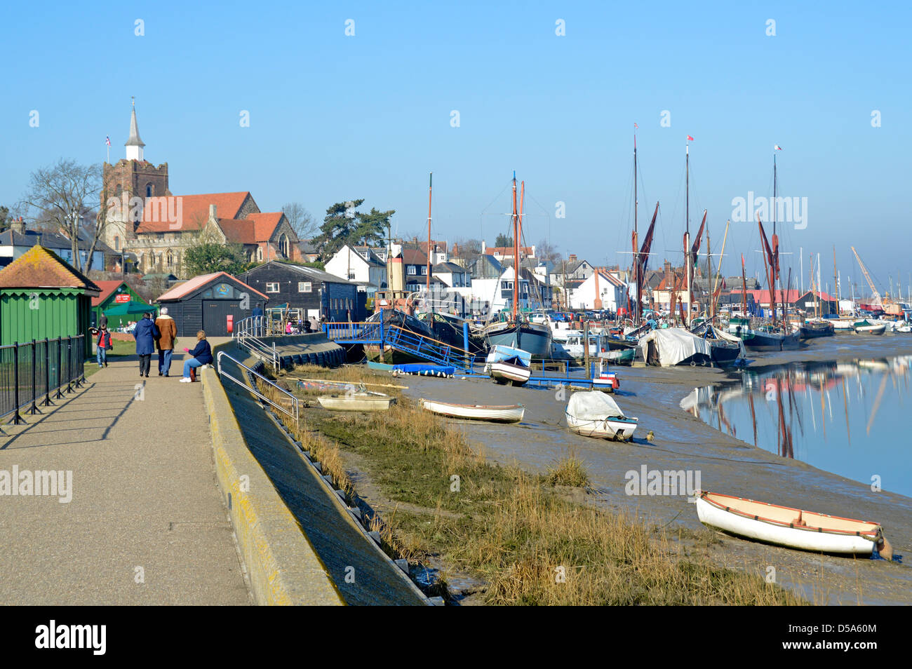 Leute, die entlang der Ufermauer spazieren, gehen am Fluss Blackwater am Hythe Quay bei Ebbe mit der St Marys Kirche hinter Maldon Essex England Stockfoto