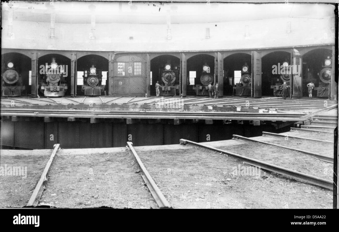 Ein Bild, das ein Roadhouse und eine Reihe von acht Lokomotiven aus dem frühen 20. Jahrhundert zeigt. Die Szene spiegelt das Wachstum von Eisenbahn und Verkehr wider, wobei der Schwerpunkt auf Technologie und Infrastruktur der damaligen Zeit liegt. Stockfoto