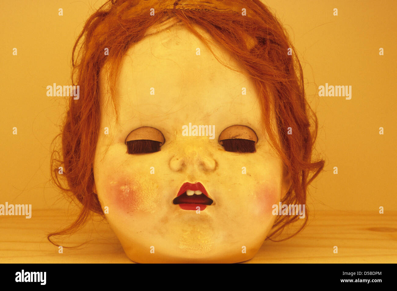 Nahaufnahme von abgenutzten Kopf des traditionellen Baby-Puppe mit geschlossenen Augen offenen Mund und unordentlich Ingwer Haare auf Holzregal Stockfoto