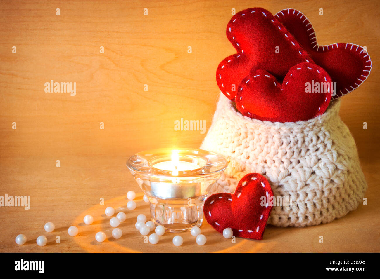Valentinstag-Konzept. Roten handgefertigte Herzen in gestrickte Tasche, Kerze und Perlen aus Holz Textur Stockfoto