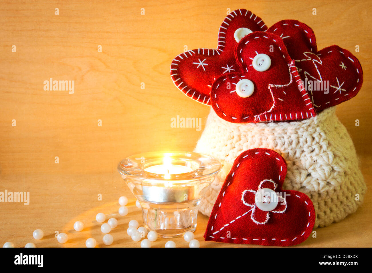 Valentinstag-Konzept. Roten handgefertigte Herzen in gestrickte Tasche, Kerze und Perlen aus Holz Textur Stockfoto