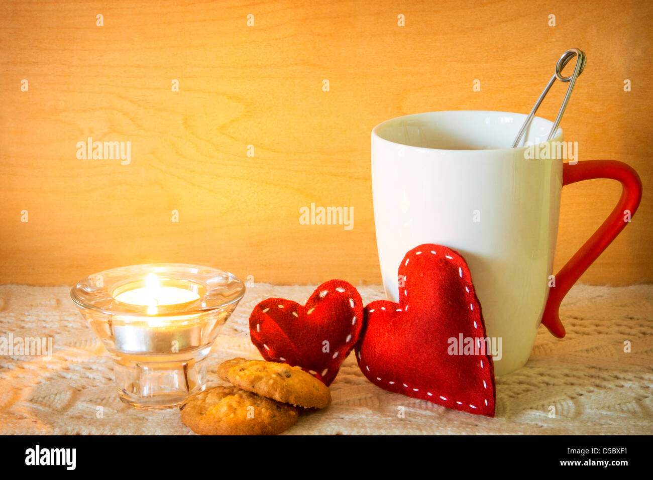 Valentinstag-Konzept. Roten handgefertigte Herzen mit Kerze und eine Tasse Tee auf Holz- und gestrickte Textur Stockfoto