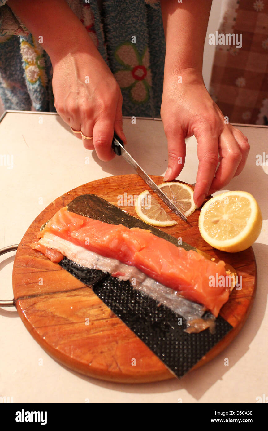 Bild von Hand schneidet Scheiben ein roter Fisch und Zitrone Stockfoto