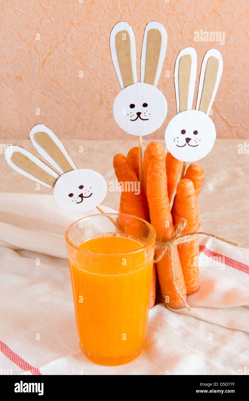 Karotten-Bündel und Saft mit Papier Kaninchen auf Leinen Hintergrund. Stockfoto