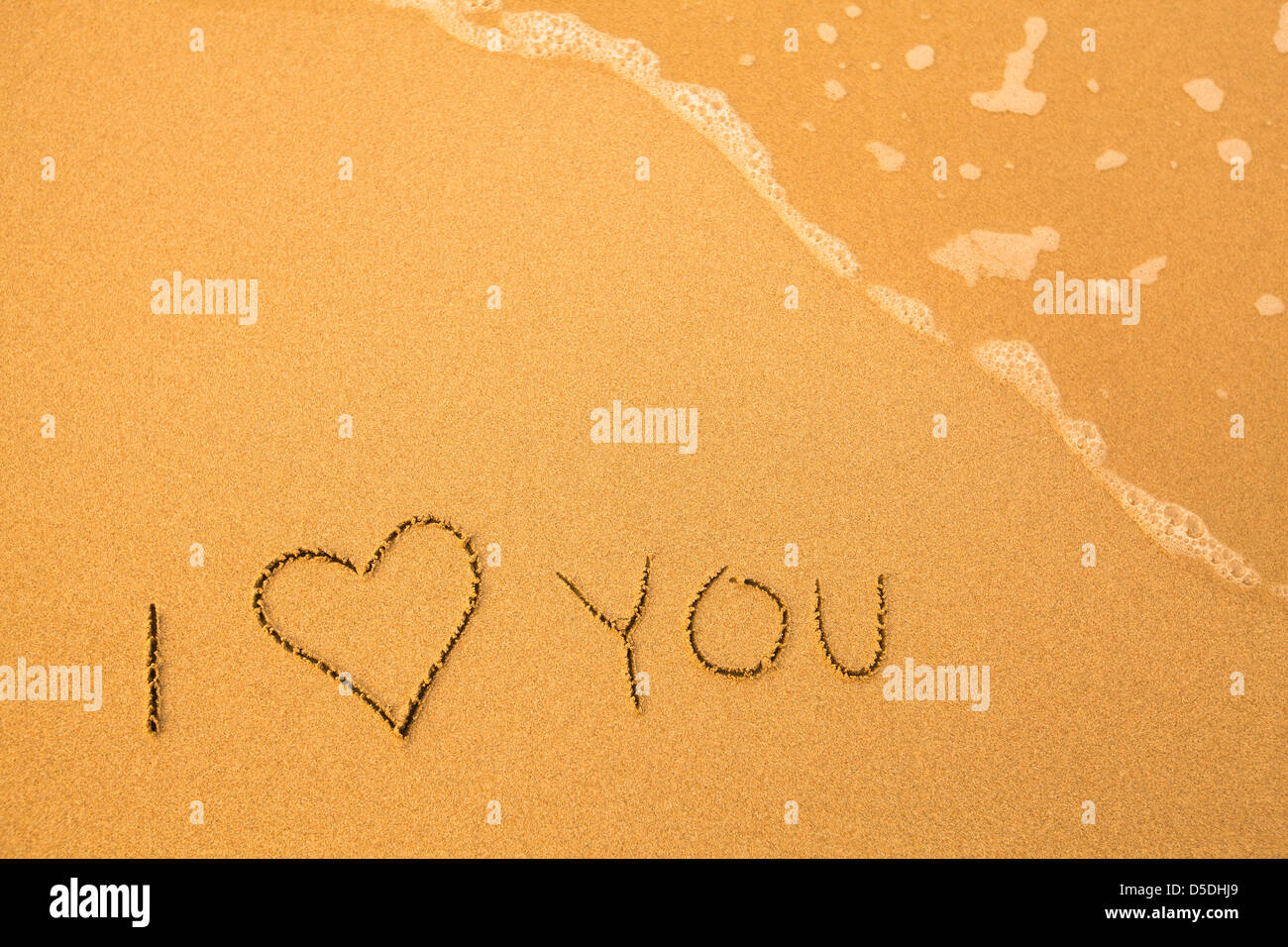 Ich liebe dich - Text geschrieben von Hand im Sand am Strand, mit einer blauen Welle. Stockfoto