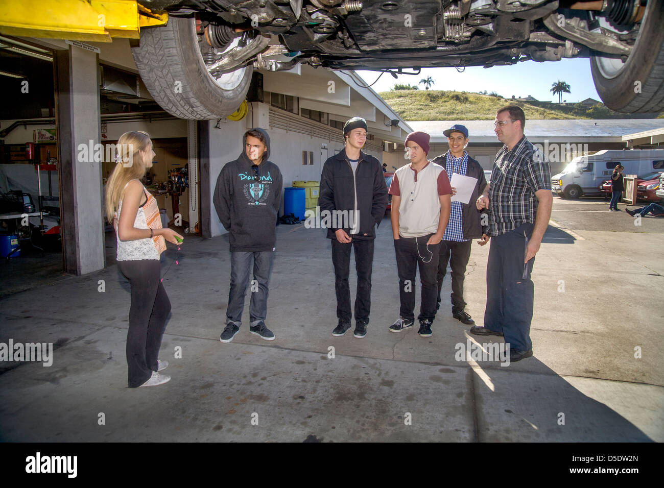 Der Lehrer eine High-School-Auto-Shop-Klasse in San Clemente, Kalifornien, weist Studenten beider Geschlechter über die Unterseite eines Autos. Stockfoto