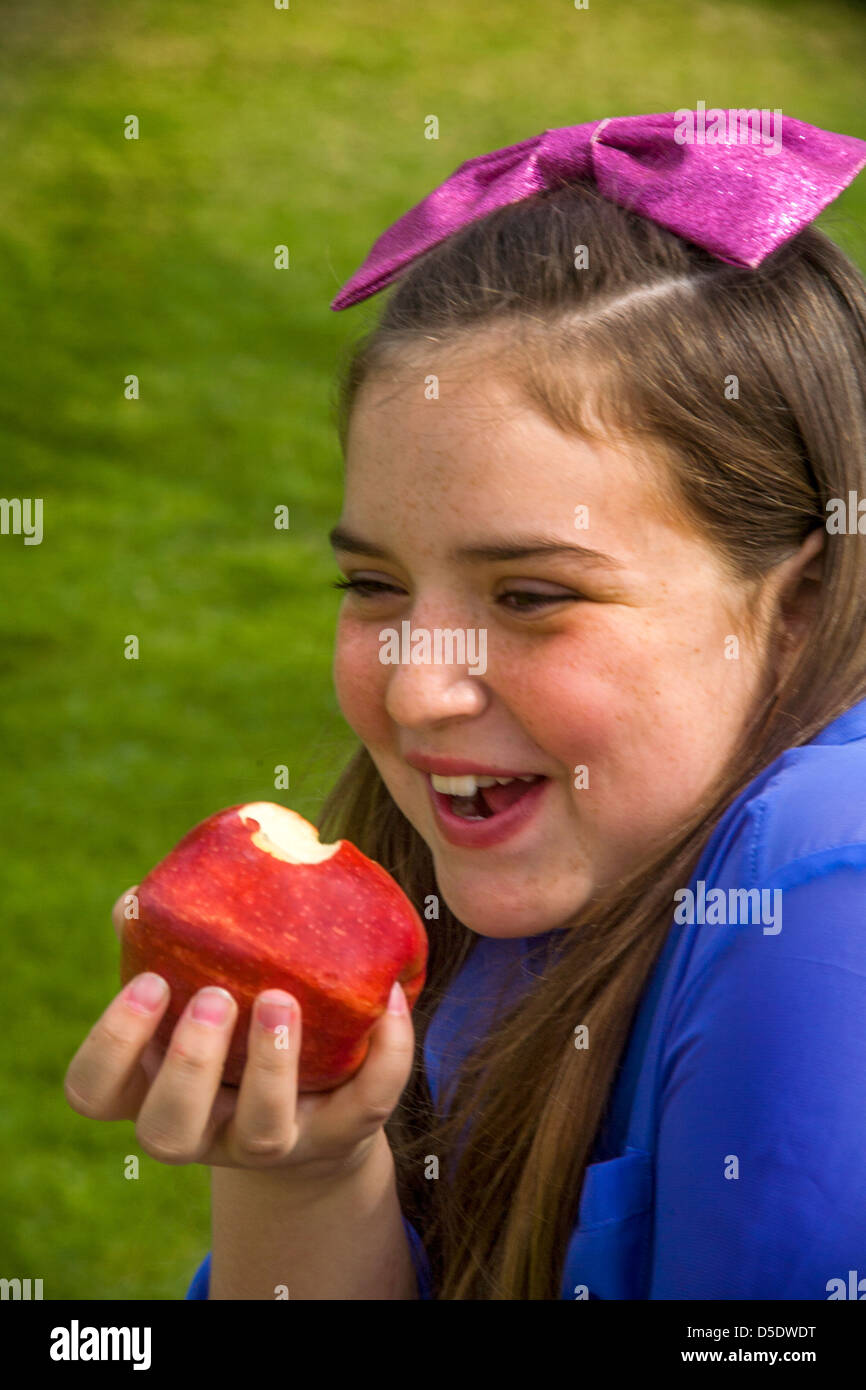 Ein fröhliches junges kaukasische Mädchen isst einen Gala Apfel im Freien in einem Lagnua Beach, CA, Park. Stockfoto